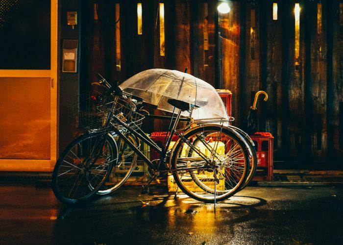 Two bicycles left out in the rain, covered by a see-through umbrella.